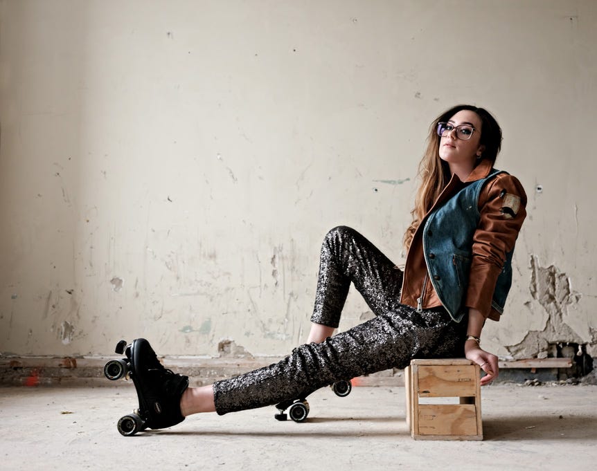 Model wearing roller skates, sitting on apple crate in derelict room