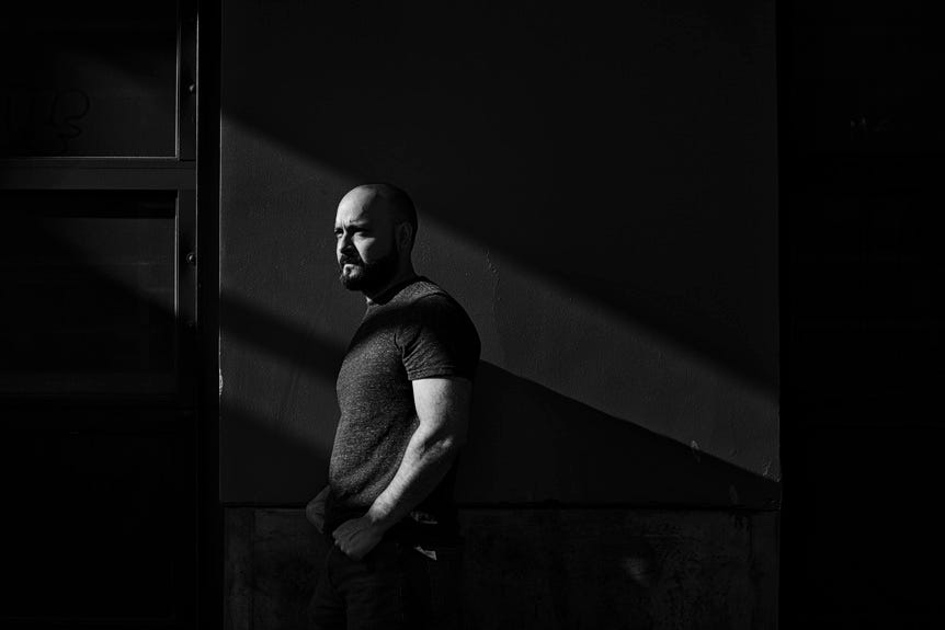 Monochrome portrait of a muscular man with beard leaning against a wall