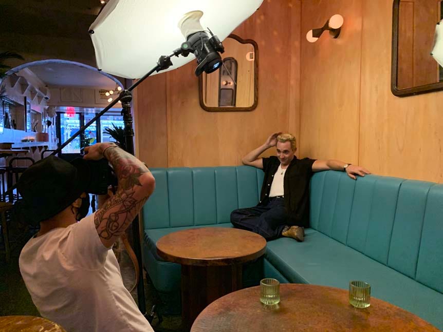 Man photographing model in vintage clothing while he sits in bar booth