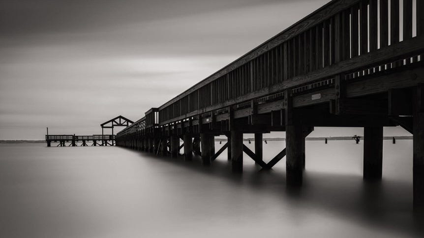 Long, wooden pier with grey skies and smooth seas surrounding
