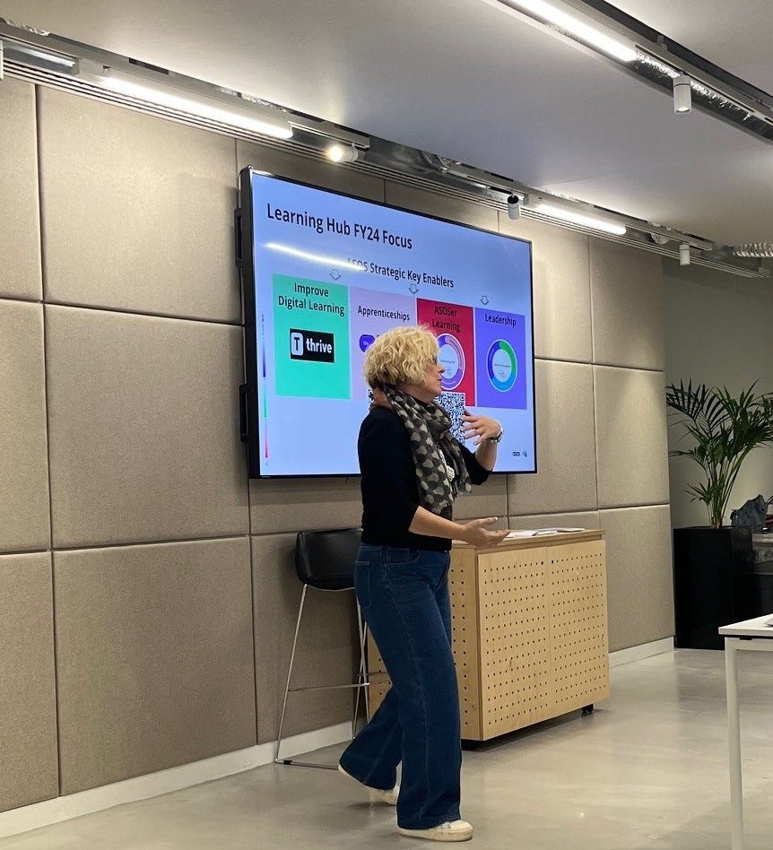 A photo of our Head of Learning, Nikki Isaac, at ASOS delivering a talk on the Learning Hub focus for FY24. She stands in front of a screen that reads ‘Learning Hub FY24 Focus’.