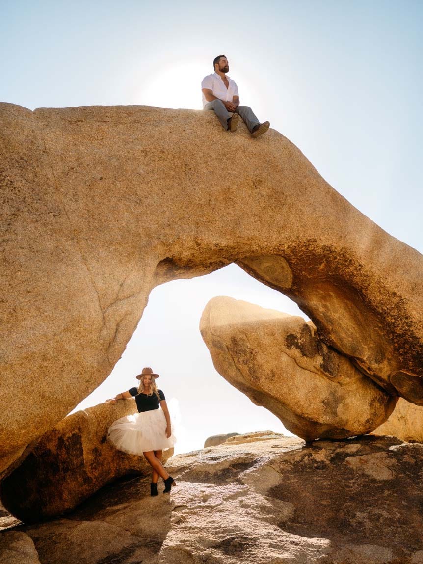 Man sitting high above woman on rocky arch in desert