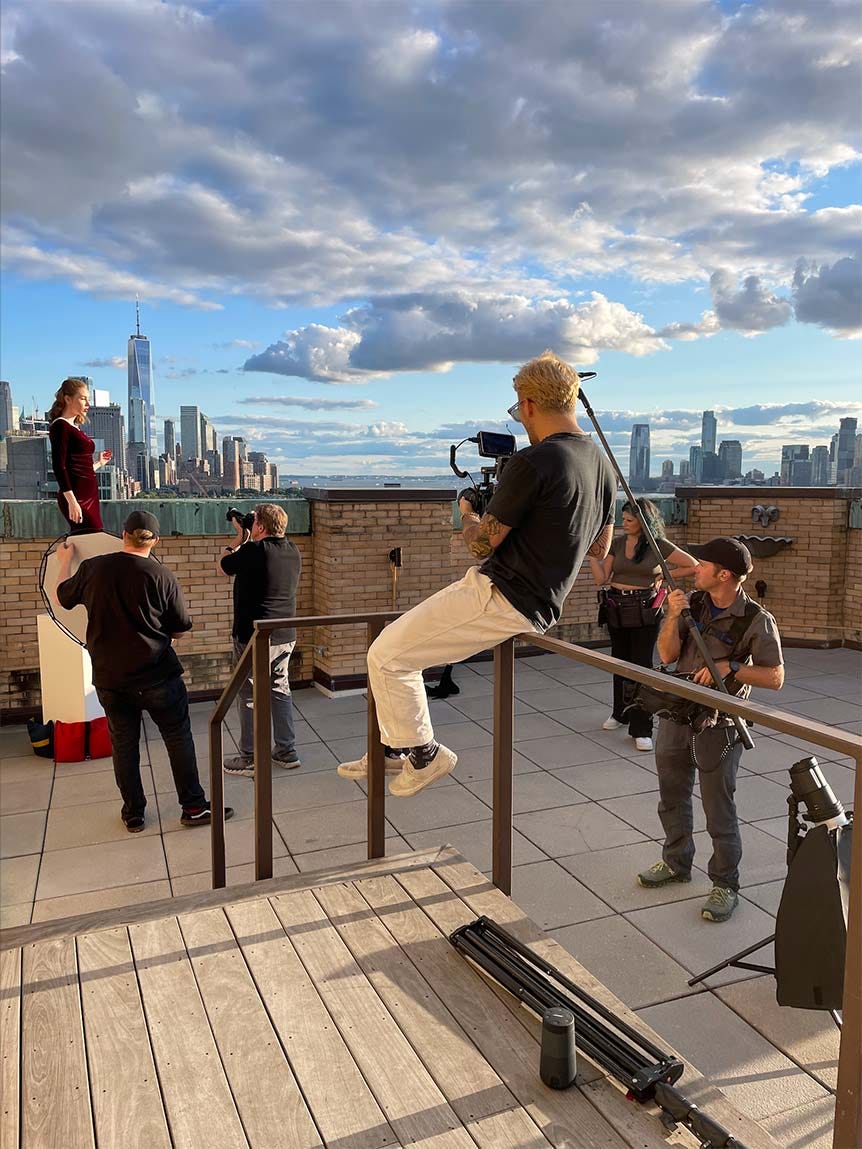 First assistant sitting on handrail on New York rooftop, with photography crew and model around