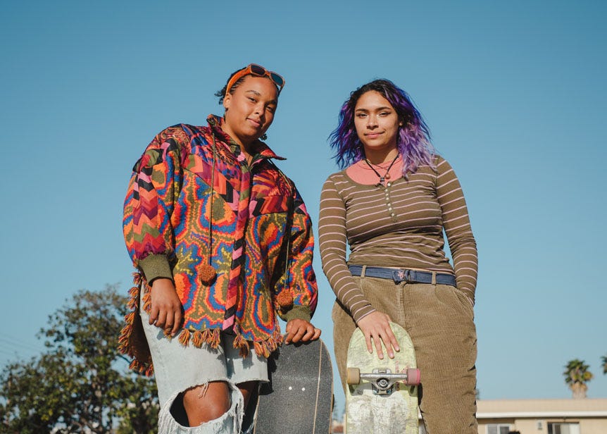 Two young woman skateboarders posing on cloudless day