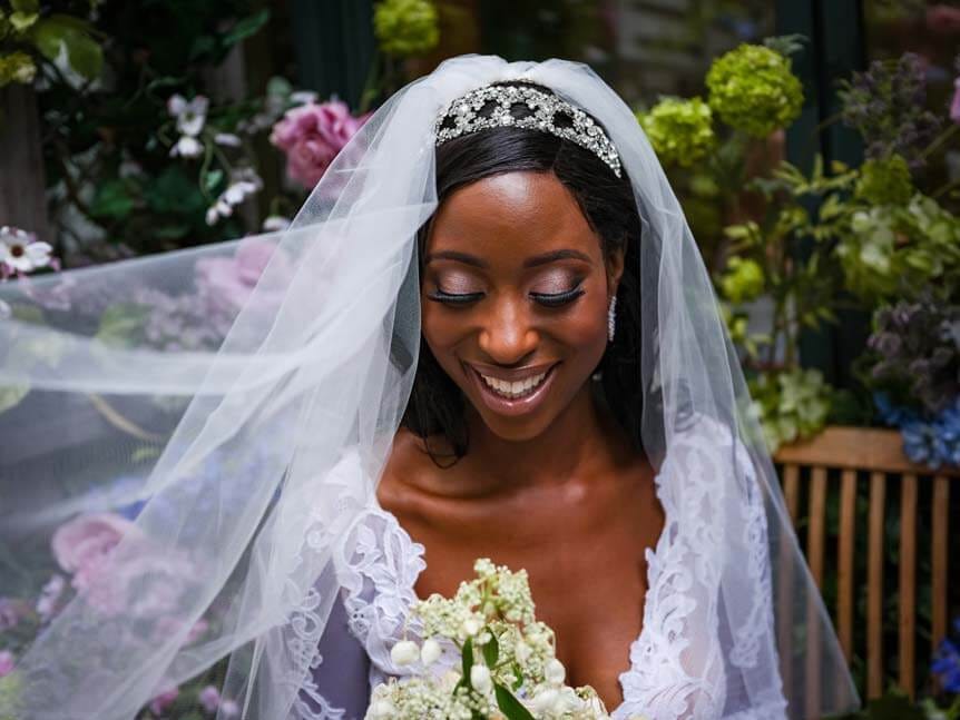 Young, African-American bride smiling against backdrop of flowers