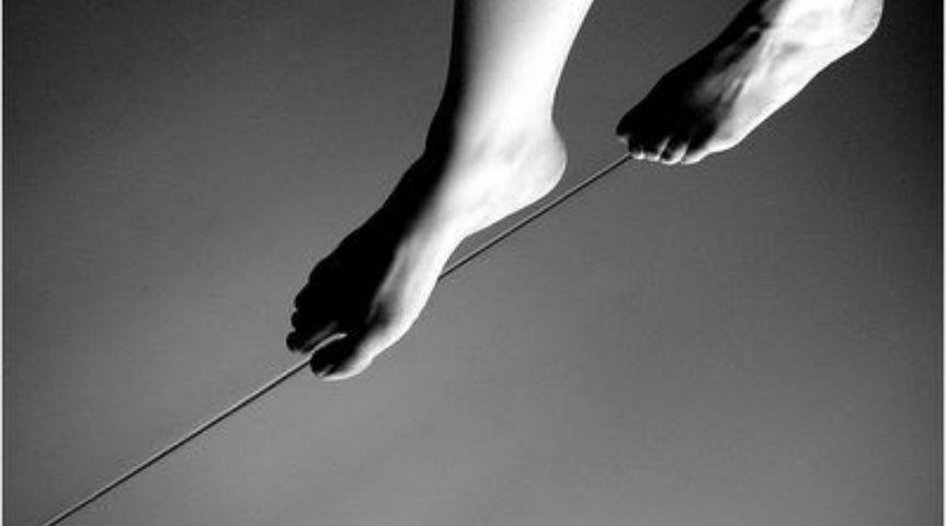 An artistic black and white photo showing a pair of bare feet delicately balancing on a tightrope, symbolizing the delicate balance between vulnerability and strength, courage and fear, and authenticity and self-protection.