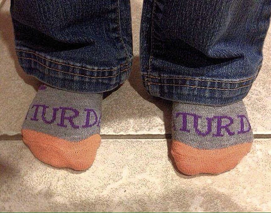 Someone wearing a pair of socks emblazoned with the word ‘Saturday’ on each, but the design means only ‘Turd’ can be seen.