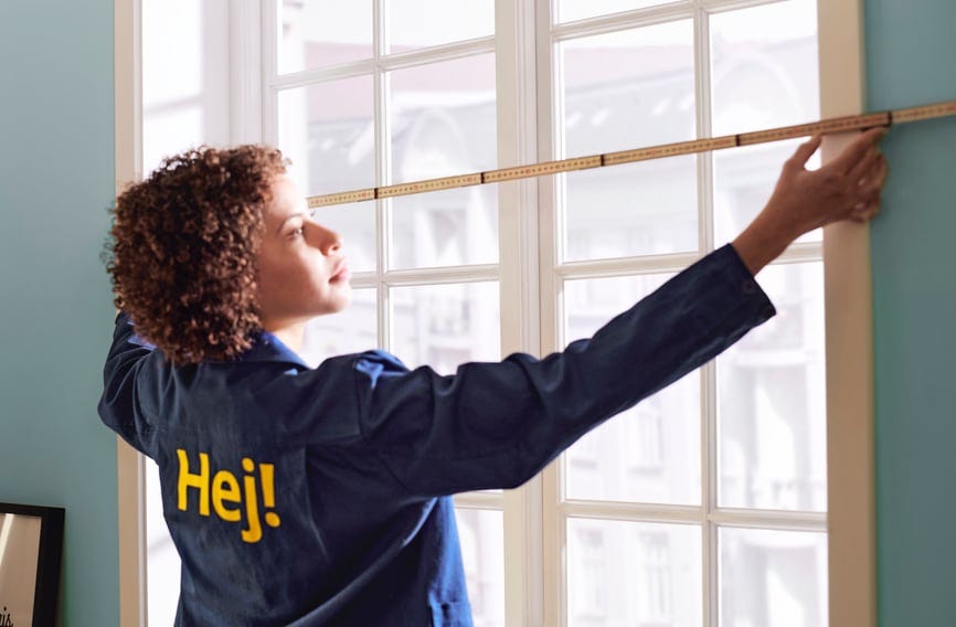 An IKEA employee measures the width of a window using a wooden measuring ruler.