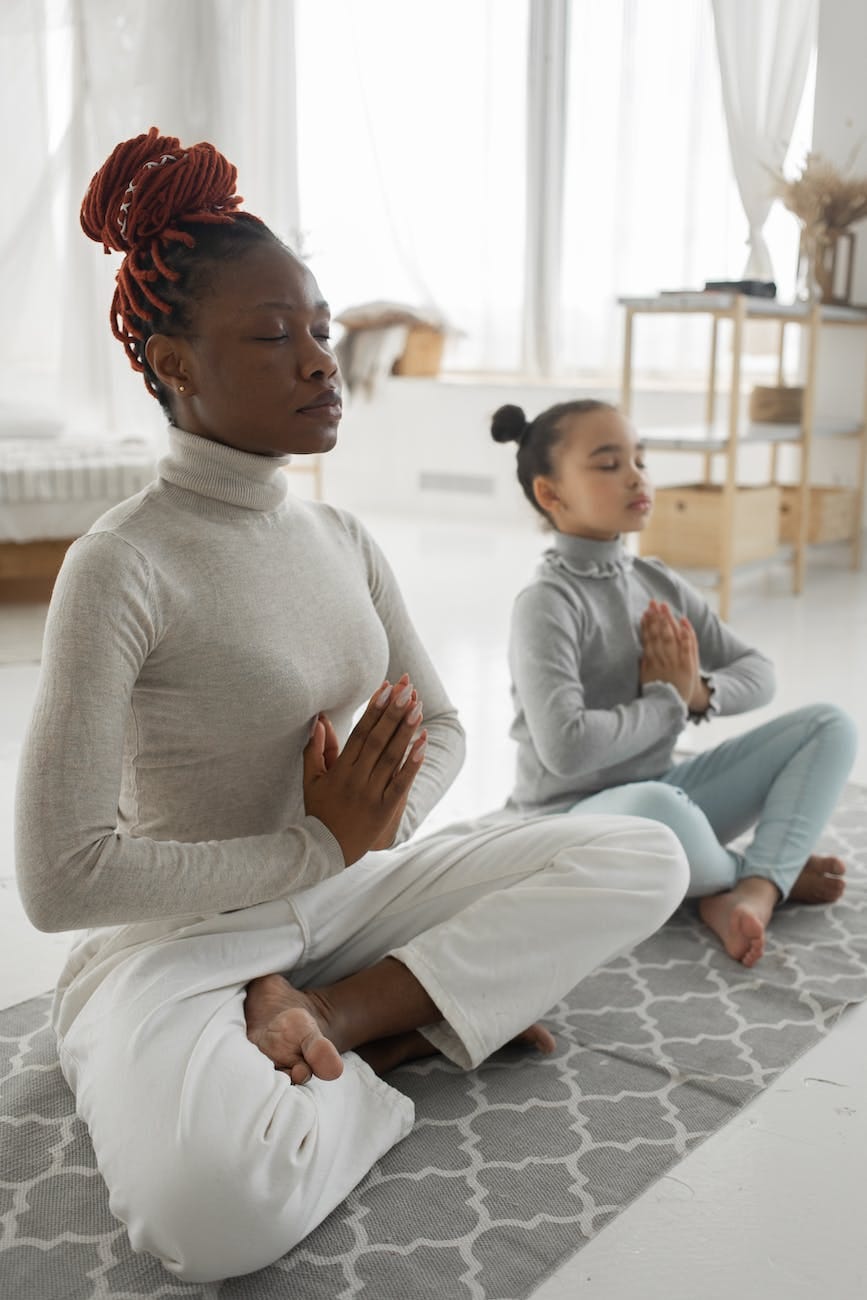 relaxed black woman with little daughter practicing lotus pose at home