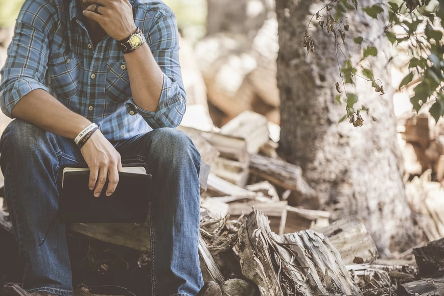 man sat on stump of wood with book in one hand