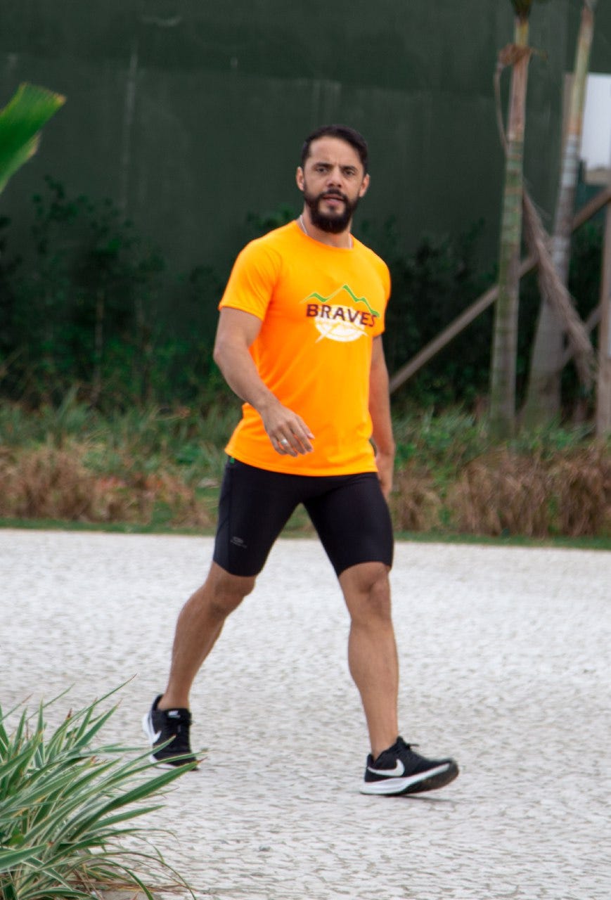 Foto do Thiago andando em direção a equipe. Ele veste a camisa da equipe, na cor laranja.