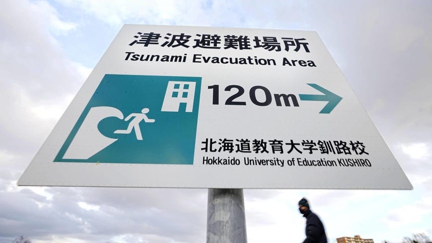 A signboard signalling a tsunami evacuation area in Hokkaido, Japan. Behind it is a silver-blue sky filled with clouds.