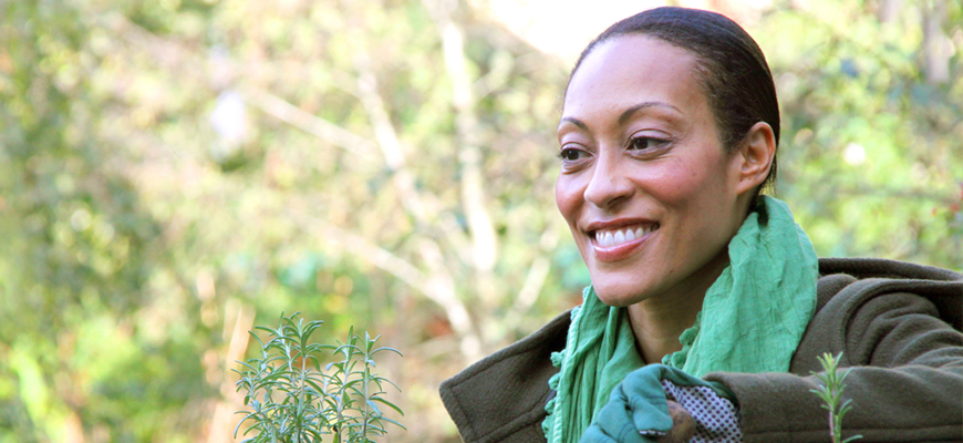 Woman in green scarf smiles off the camera with a background of trees.