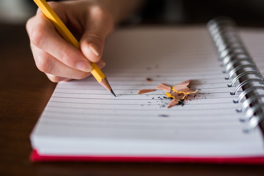 A hand writing onto a blank notebook with a yellow pencil