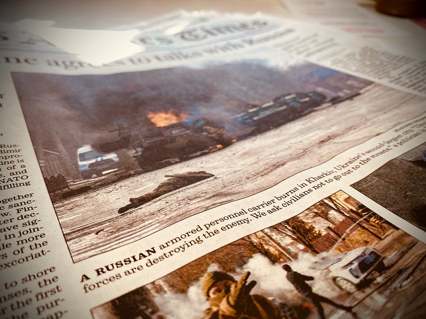 Photo of a newspaper front page of the LA Time Feb 28, 2022. Burning armored vehicle in city street and body lying on street.