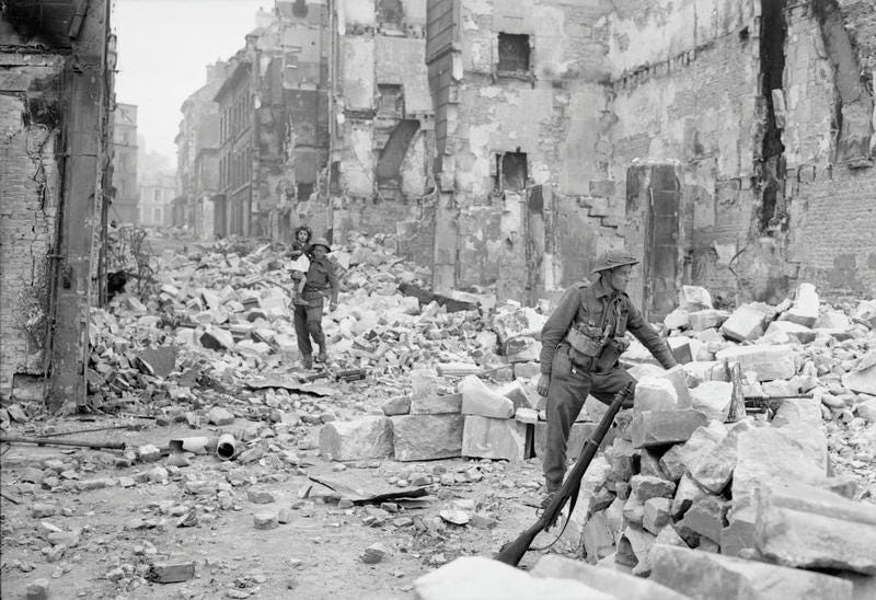 1944 — British soldiers in completely ruined town in Normandy. One soldier holding a baby. Black and white.