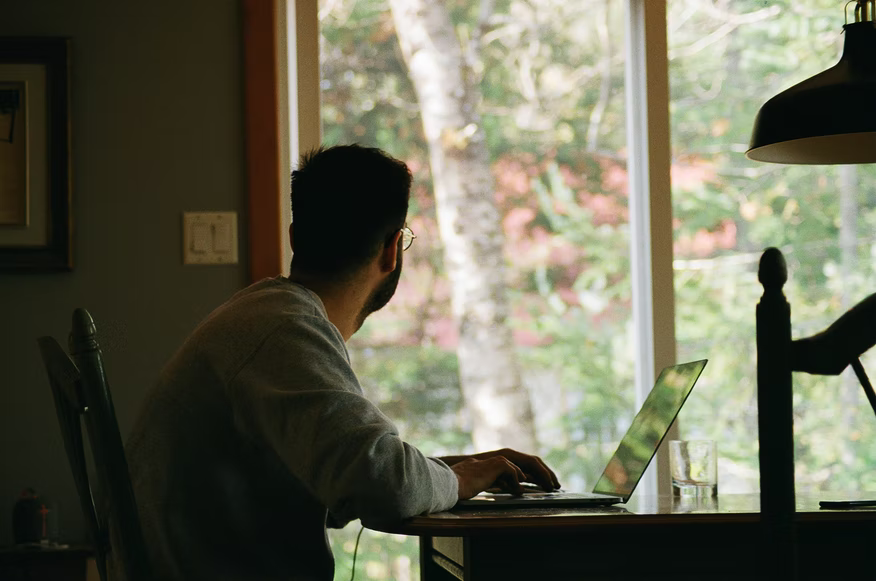 Homem sentado em frente ao notebook olhando pela janela home office — como instalar o maven no mac