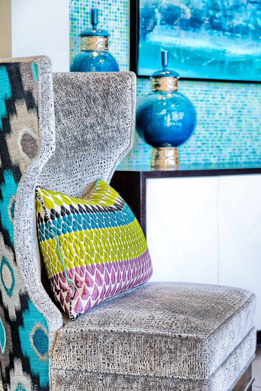 A textured chair in front of a tiled wall with a blue vase.