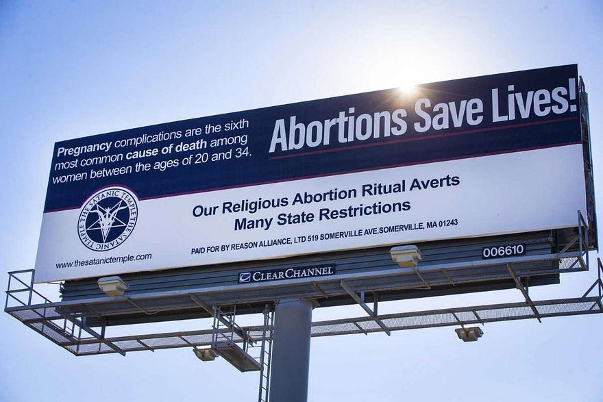 Satanic Temple billboard that says “Our religious Abortion Ritual Averts Many State Restrictions” and “paid for by Reason Alliance Ltd., 519 Somerville Ave, Somerville MA 01243”