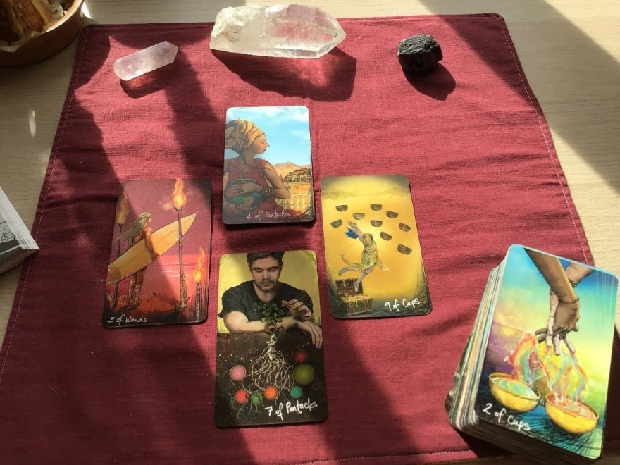 A red Tarot cloth with 4 Tarot cards layed out on it, next to a pile of Tarot cards.