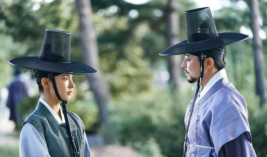 Two people dressed in ancient Korean (Joseon) clothes talk standing opposite each other