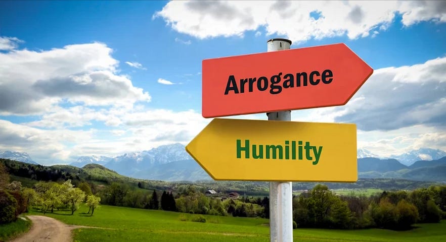 A street sign with arrows pointing in opposite directions. One is labeled “Arrogance” and the other “Humility”.
