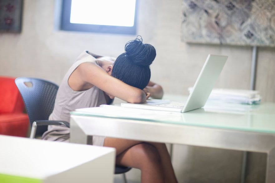 A photo of a person at a desk with their head down in front of a laptop