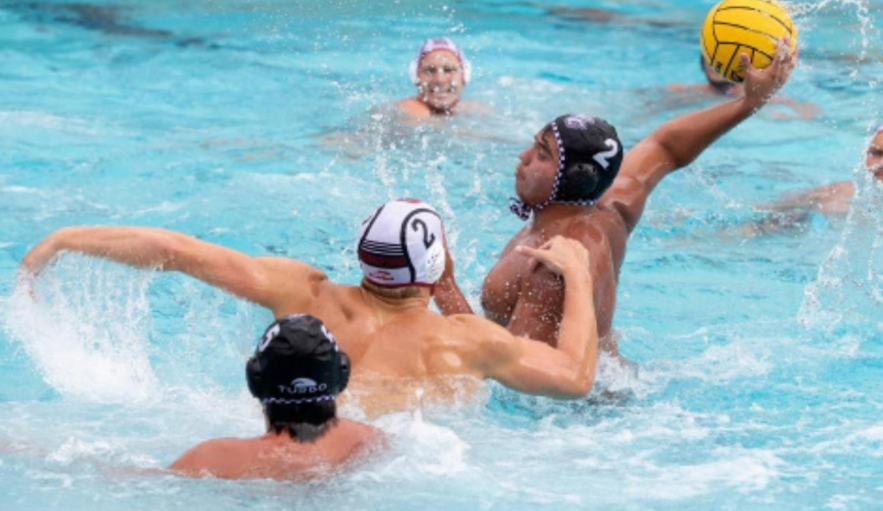 A player on the Men’s Waterpolo team is aiming to throw the yellow waterpolo ball while the opposing team member pulls on his sholder.