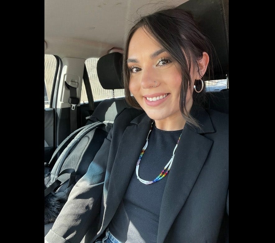 Lorell Ward sits in a car and smiles at the camera, wearing a beaded necklace and black blazer