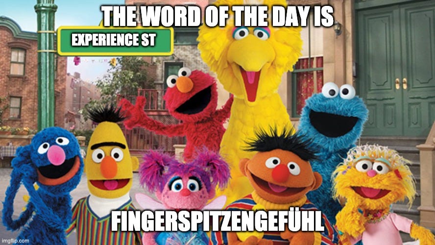 Various Muppets from the show Sesame street are smiling with a top caption “The word of the day is” and a bottom caption “Fingerspitzengefühl”. The text in street sign says “Experience St” rather than Sesame St.