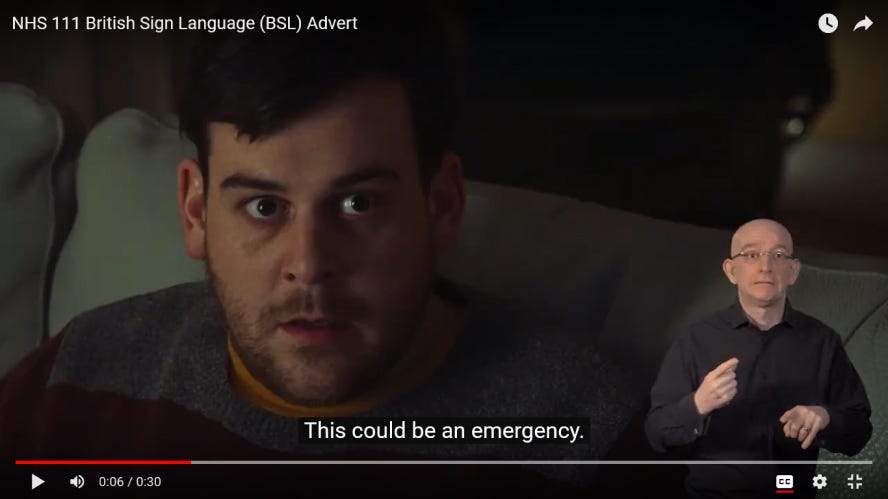 A YouTube video showing someone sitting on a couch having a fearful look on their face. A sign language interpreter is shown in the bottom-right corner of the video. The closed caption of the video currently reads: “This could be an emergency.”