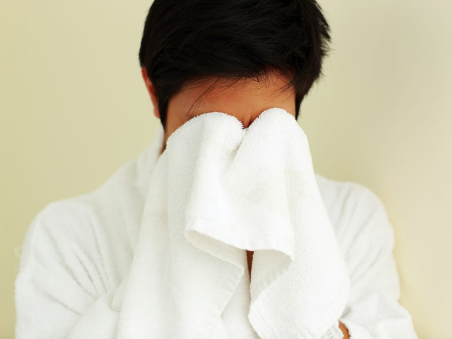 A person pats their face with a washcloth.