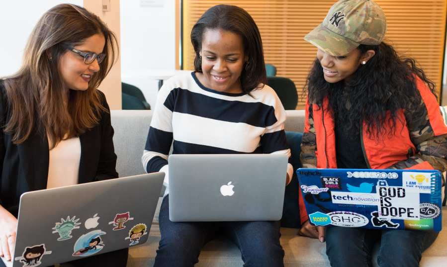 Three young women with laptops working together.