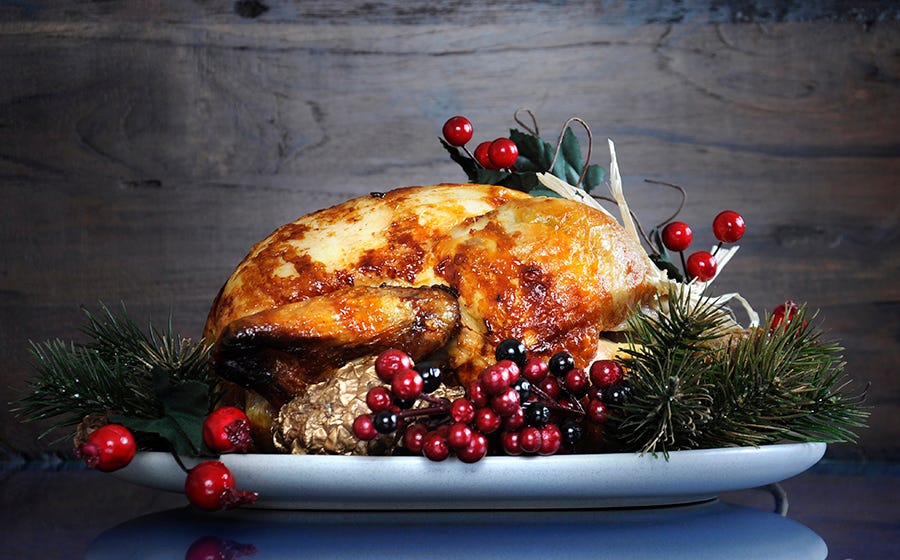 Scrumptious roast turkey chicken on platter with festive decorations for Thanksgiving or Christmas lunch, against dark recycled wood background.