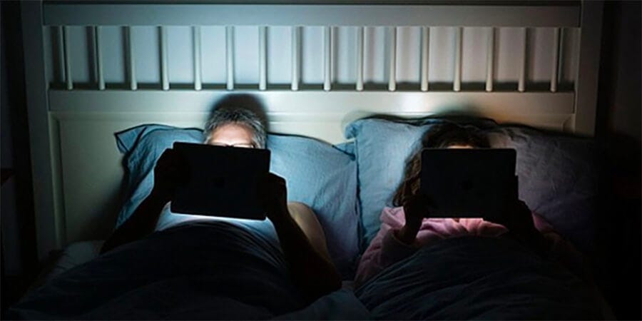 Couple in bed staring into very bright tablet screens.