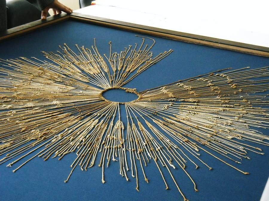 A gold circle of thread with long threads with knots on them connected to it, called a quipu