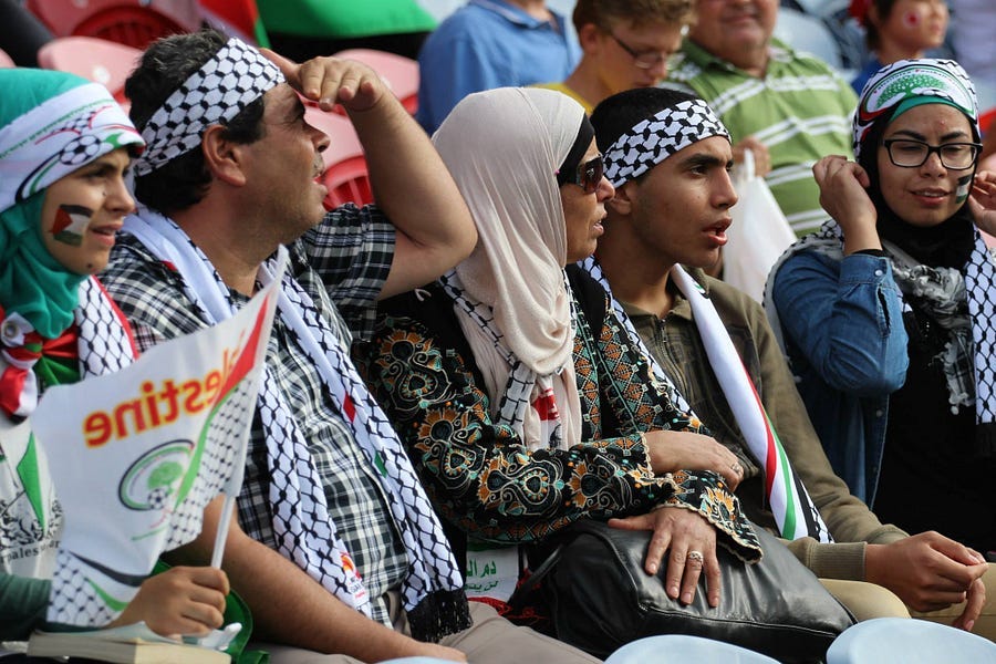 Football suppoerters carrying Palestinian flags and wearing Palestinian fan gear