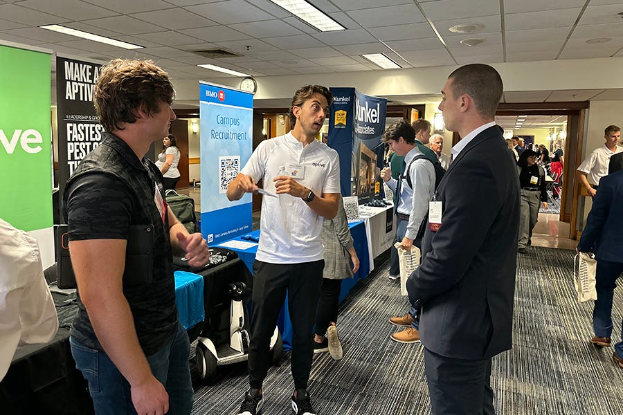 Three men talk to another during a career fair.