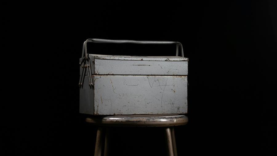 A metal toolbox sitting on a chair with a black background
