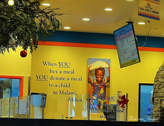 Photo of the walls at Malawi’s Pizza in Provo with words written — When you buy a meal, you donate a meal to a child in Malawi, Africa. there is also a screen showing their menu…