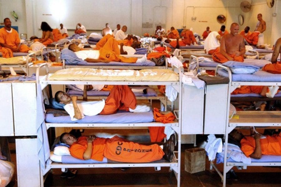 Overcrowded prison dorm, with dozens of inmates in bunks stacked three beds high.