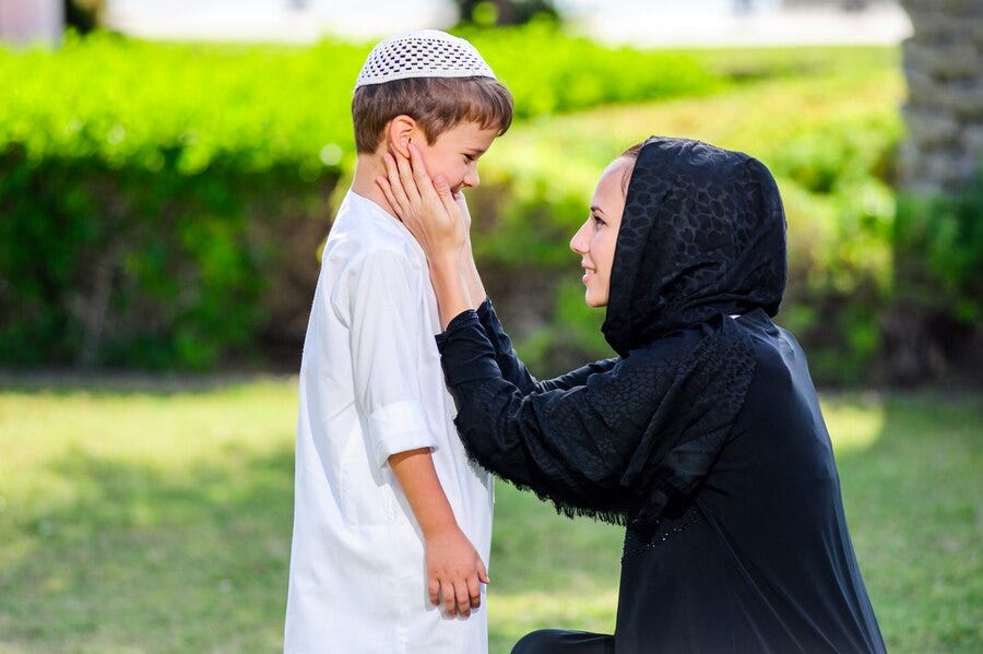 A mother kneeling in front of her young son, gently caressing his face with a tender expression