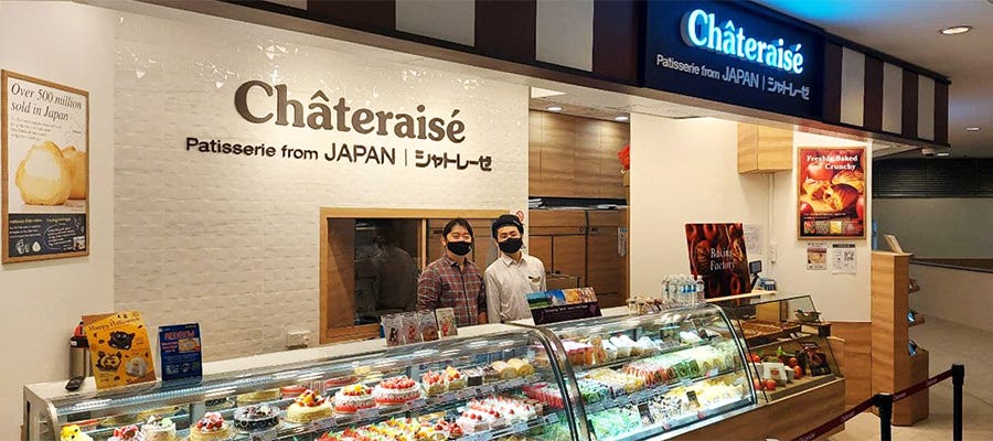 A photo of Châteraise’s store front with cakes in chiller and 2 guys wearing masks.