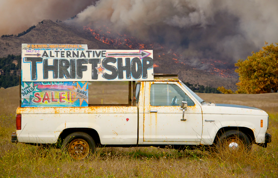 a truck with a sign to a thrift store sits in a field in front of a wild fire