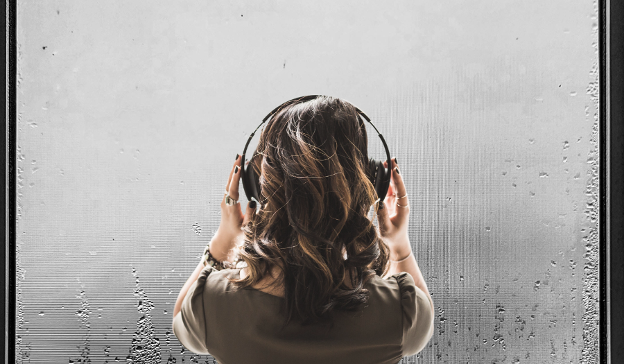 An introverted young woman wearing headphones as she stands by a misty glass window, looking out. The image showcases the solitude and introspection of an introvert.