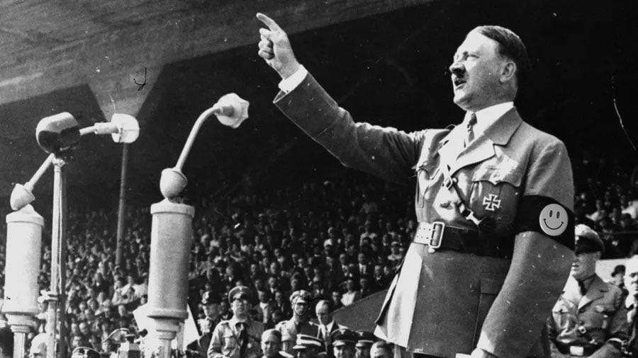 Hitler speaks from the tribune, his swastika is covered by a smiley face