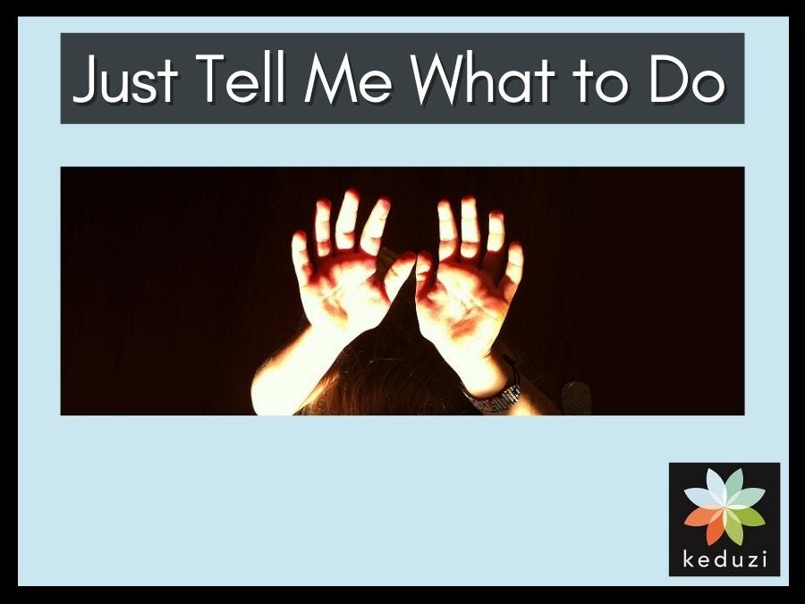 A child’s hands are raised up and lit up against a dark backdrop. You can barely see the top of a head and a bracelet on one wrist. The words over the image are “Just Tell Me What to Do”. The Keduzi logo, which is a colourful flower, is also over the image.