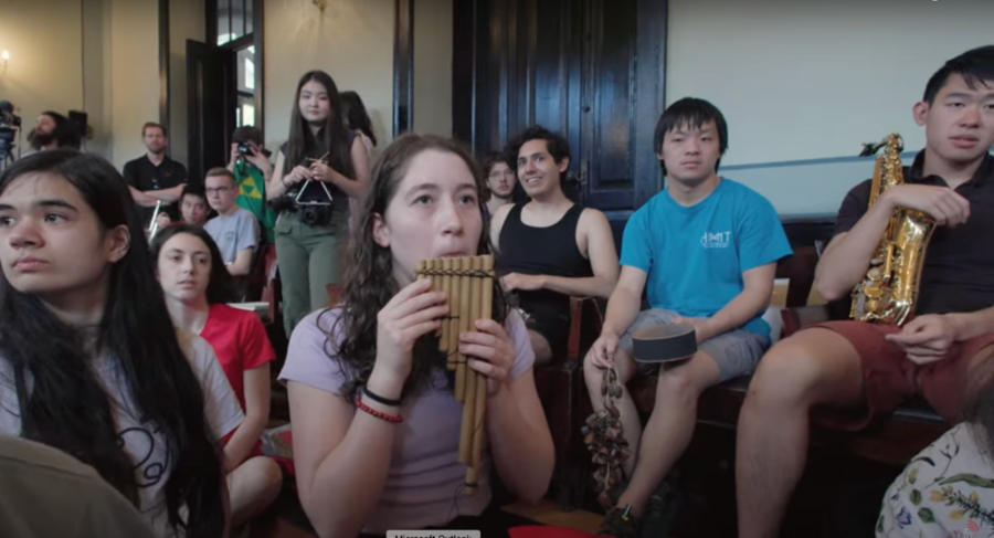 MIT students and others sit together, several holding or playing musical instruments.