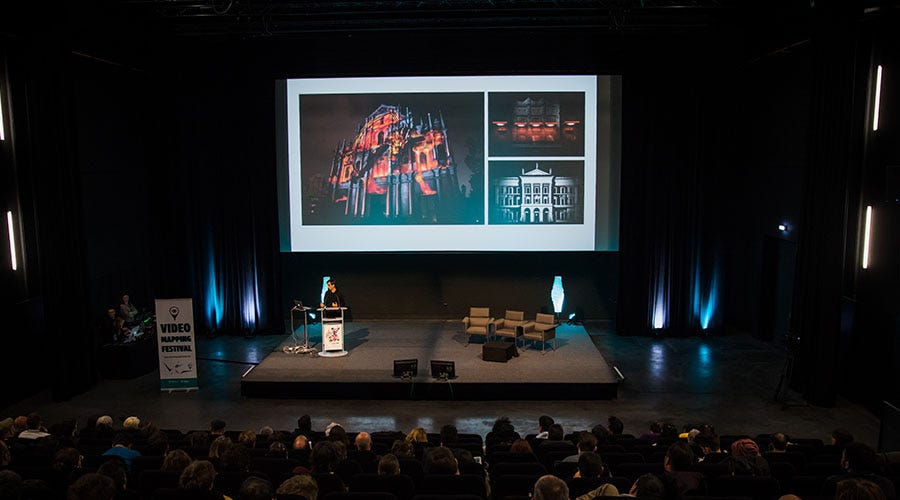 Conference stage with an audience and large screen.