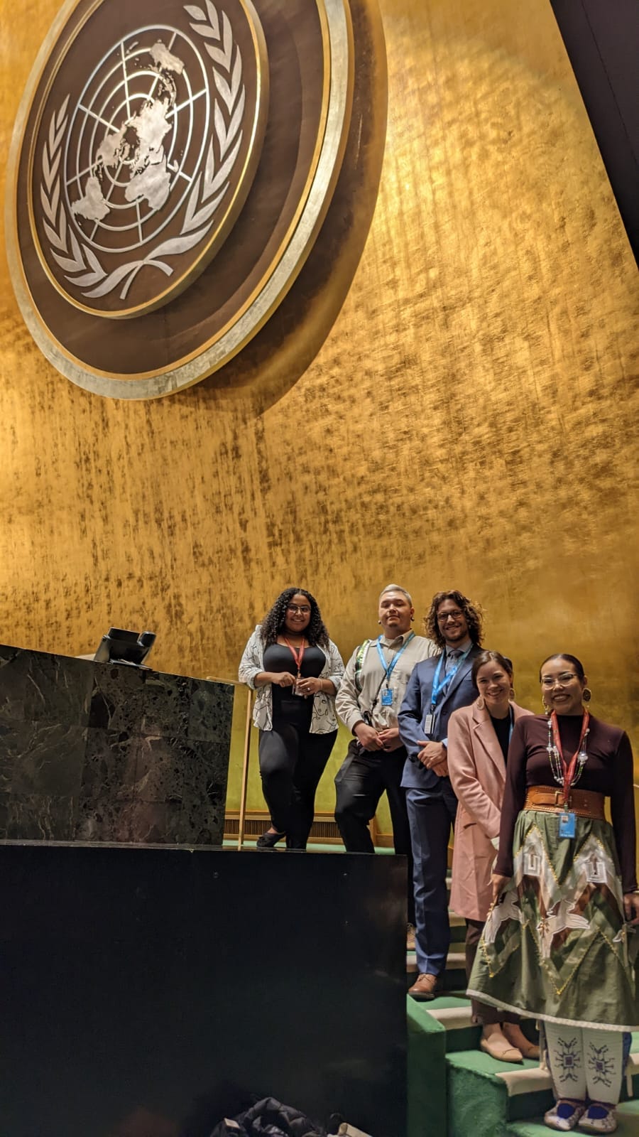 Youth pose on stairs beneath the United Nations logo at the UN headquarters in New York City.